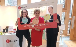 Nicola Sturgeon and hey girls staff in a hey girls photo frame next to a display stand with products